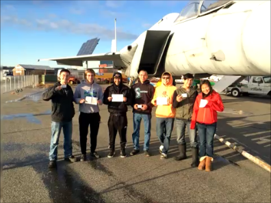 Aviation students in Anchorage standing in front of an F-15 fighter jet at the Alaska Aviation Heritage Museum holding their third class medical certificates.